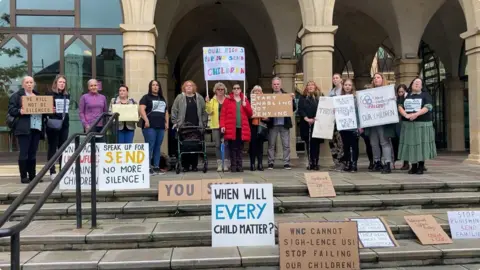 BBC Group of parents holding banners outside meeting