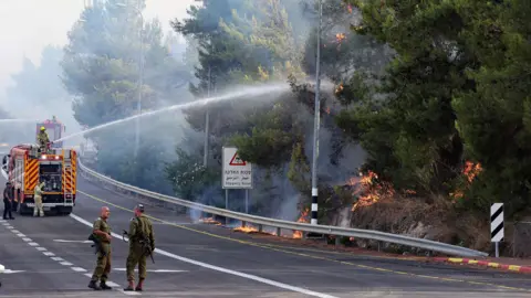 Getty Images Soldiers stand near a fire engine spraying water on a forest fire