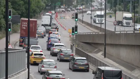 Two long lines of traffic stretch into the distance with traffic cones and lane closure signs close off a main road into a busy city centre