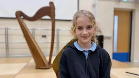 A young girl wearing school uniform smiles at the camera