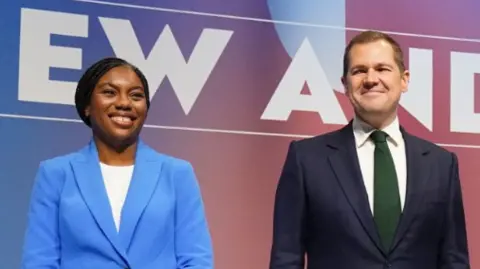 Tory leadership candidates Kemi Badenoch (L) and Robert Jenrick (R) stand side by side on a stage during the contest.