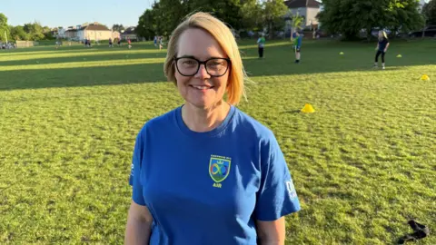 Louise Sims in front of the AIR team training pitch in a blue Kingswood AIR t shirt.