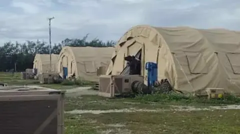 Three large tents are provided standing in a row on a grassy area in Diego Garcia