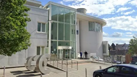 A large light-coloured building with a floor to ceiling glass entrance.