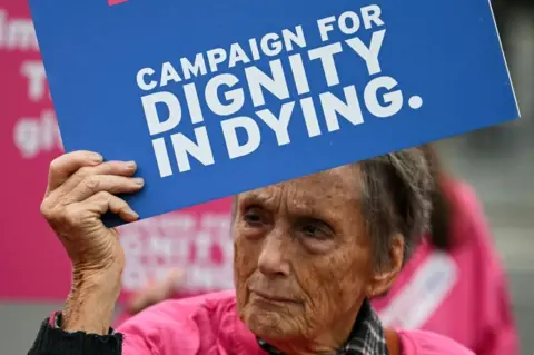 Getty Images A campaigner from "Dignity successful  Dying" holds a placard during a objection  extracurricular  The Palace of Westminster, location  to the Houses of Parliament