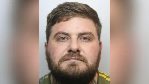 South Yorkshire Police A mugshot of Cotton, who has a brown beard, blue eyes and medium-length brown hair. He is wearing a khaki top with yellow strips along his shoulder. It appears he has a tattoo around his neck.