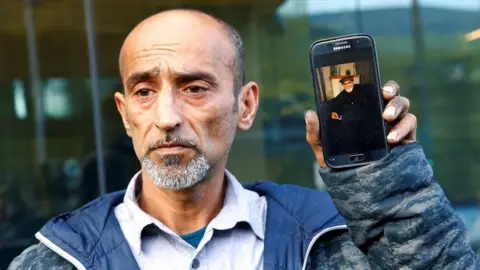 Reuters Omar Nabi holds a phone with a picture of his father Daoud, who died in the Christchurch mosque shootings (16 March)