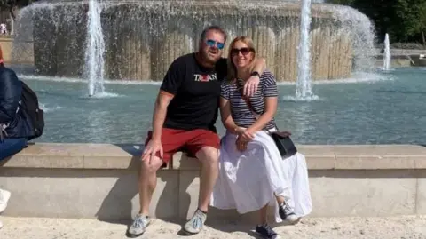 Carol Joy A man and a woman sit on a wall in front of a fountain. 