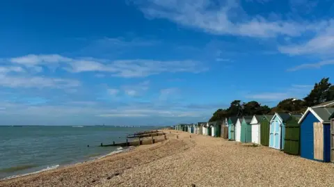 Beach huts and groynes on a stony beach near Lee-on-the-Solent in the sunshine.