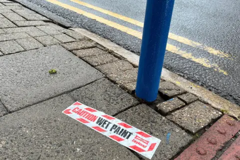 Photo of pavement with  'CAUTION WET PAINT' sticker surrounded by blue paint