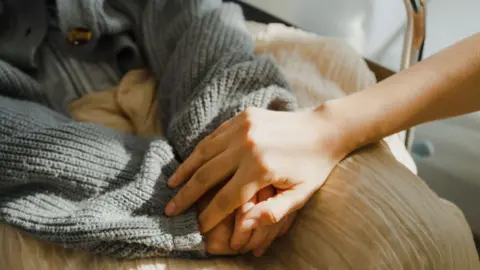 A person placing their hand on top of someone's hands that they have put together on their lap.