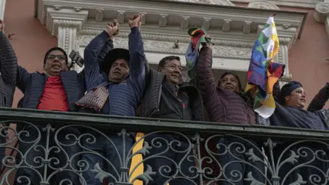 Bloomberg/Getty President Luis Arce stands holding hands with people on a balcony