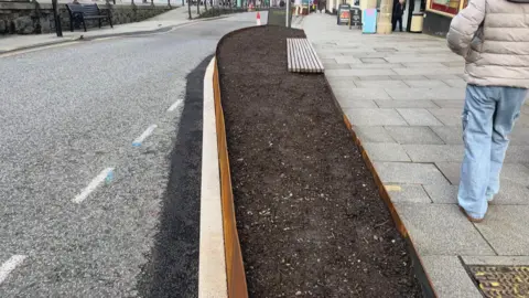 A long planter on the edge of a pavement in Penzance. The exterior is rusty - Inside is bare earth before plants go into it.
