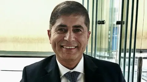 Quzmar family Head and shoulders shot of Jihad Quzmar, wearing a tie and jacket and smiling towards the the camera