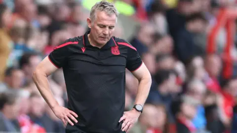 Phil Parkinson looks to the floor with his hands on his hips on the sidelines during a Wrexham game 