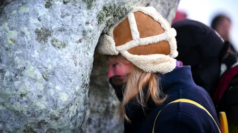 Getty Images A woman rests her head against one of Stonehenge's stones in a moment of quiet contemplation.