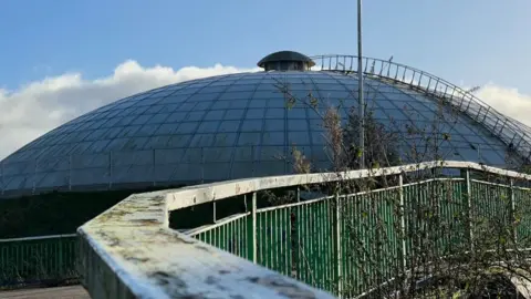 A close up of the dome of the leisure centre, with railings in the foreground.