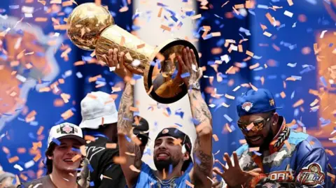 REUTERS/Dylan Martinez New York Knicks' Jose Alvarado holds up the NBA championship trophy with Tyler Kolek, Karl-Anthony Towns and the Larry O'Brien Championship Trophy at New York City Hall during the parade 