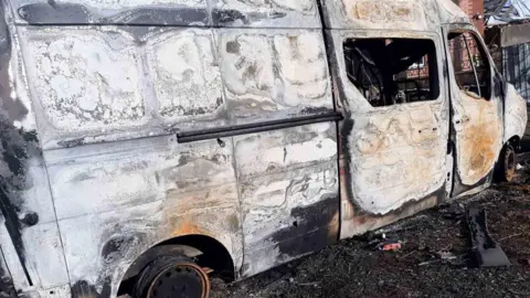 Vlad A damaged white van on a black burnt ground.