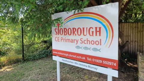 Stoborough Primary School A sign outside the school which is white and red with a rainbow design on. It says Stoborough CE Primary School