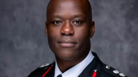 Wayne Brown, West Midlands Fire Service, in his firefighter uniform in front of a gray wall