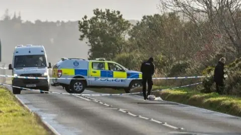 Police on road with police vehicles and police tape and officers looking in bushes