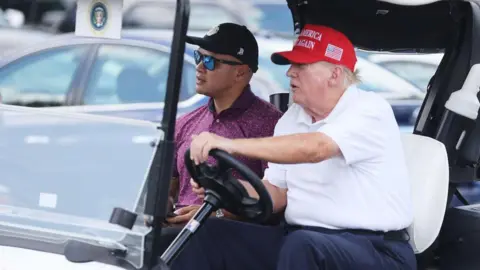Getty Images Donald Trump drives a golf cart, accompanied by aide Walt Nauta