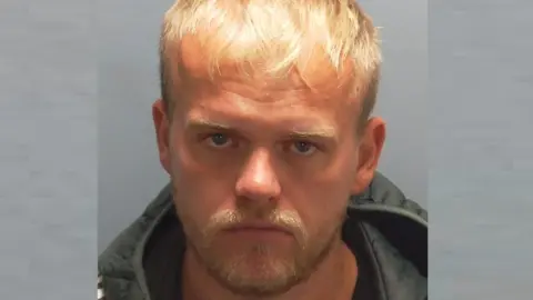 Hampshire and Isle of Wight Constabulary In a police custody photo, Charlie Jeans face the camera wearing a sombre expression. He has blonde hair and a beard and wears a padded jacket or coat.