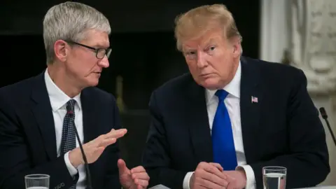 Tim Cook, chief executive officer of Apple Inc., left, speaks while US President Donald Trump listens at a White House meeting in 2019