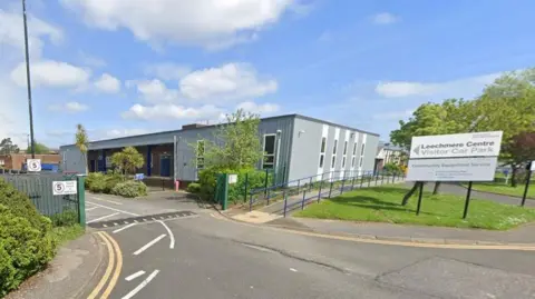 Google A sign for Leechmere Centre car park, with the centre at the back. It is a grey one-storey building. 