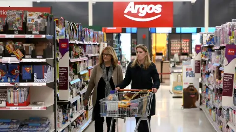 An Argos logo is seen inside a Sainsbury's store as two people walk down an aisle pushing a trolly