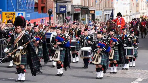 PA Media A band of pipers is followed by a man on horseback, wearing a red jacket