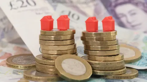 PA Media Piles of pound coins on top of bank notes, topped with four red Monopoly houses