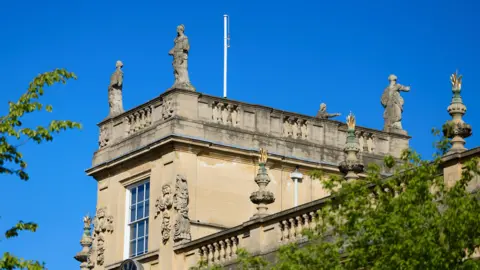 Trinity College Four statues atop a tower sit against a bright blue sky