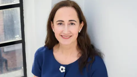 Sophie Kinsella pictured in 2018, standing against a white wall and window