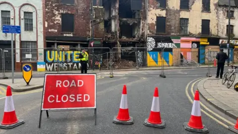 Oli Constable/BBC Exterior shot of some crumbling, derelict shop fronts in Leeds city centre with a road closed sign and traffic cones