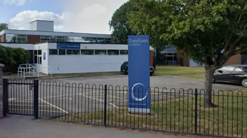 A blue pillar sign in grounds behind railings says Fareham Academy.
