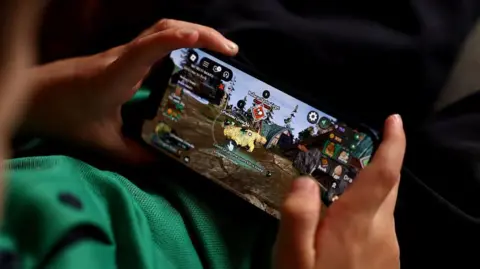 In this photo illustration, a young child holds an iPhone while using the online game platform Roblox 