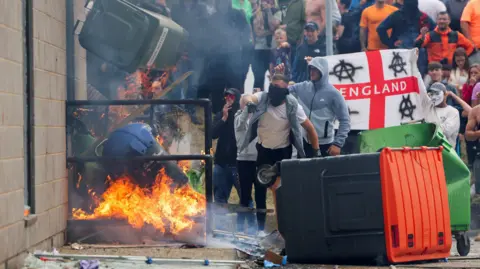 Reuters Protestors throw a garbage bin on fire outside a hotel housing asylum seekers in Rotherham, England on 4 August 2024 