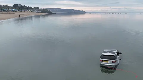 SWNS Drone photo of the stranded 4x4 with the sea up to its wheel arches