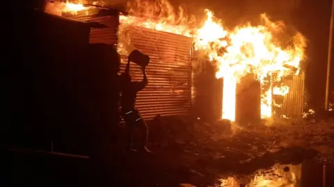 Enoch David/Reuters A person attempts to extinguish fire on a building after the volcanic eruption of Mount Nyiragongo, which occurred late on 22 May 2021, in Goma, Democratic Republic of Congo