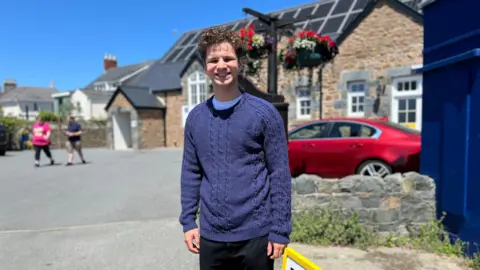 Young man with brown curly hair in a home knitted navy coloured jumper.