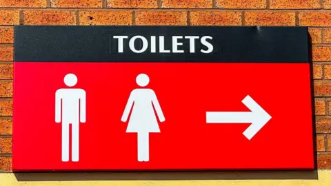 A large red sign with white lettering which reads Toilets, with a picture of a man and a woman below it