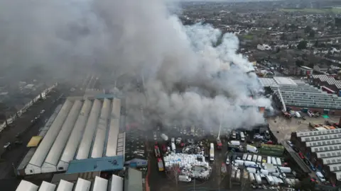 Drone footage of large smoke plumes coming out of a factory due to o a fire at an industrial building