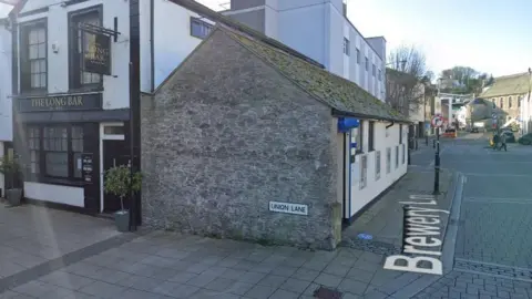 Google Street View image of the public toilets at the end of Union Lane in Brixham. A Union Lane road sign is on the end gable wall of the block. A pub called The Long Bar is just behind the toilet block.