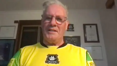 A man with glasses in a yellow football jersey.