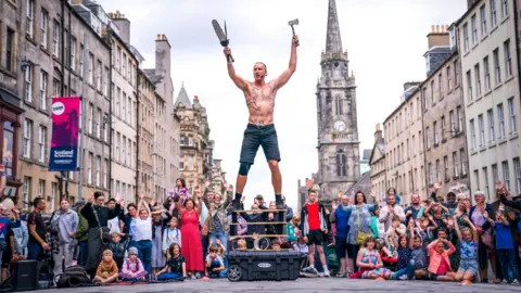 A bare-chested male street performer in front of a crowd on Edinburgh's Royal Mile.