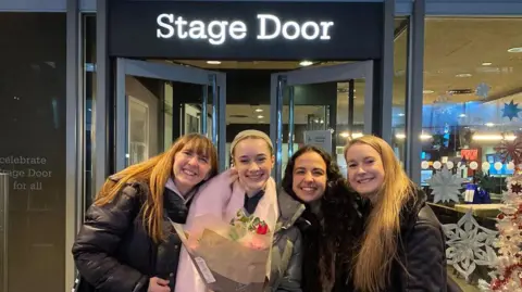 Cops Copley A young girl holding a bunch of flowers stands beaming next to three other women who have their arms around her