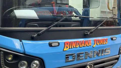 Torridge District Council Council The front of a blue bin lorry with "Bindiana Jones" written in bright yellow to red ombre lettering in the font of the Indiana Jones movies 