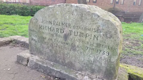 A wide gravestone saying "John Palmer otherwise Richard Turpin the notorious highwayman and horse stealer executed at Tyburn April 7th 1739 and buried in St George's Churchyard".